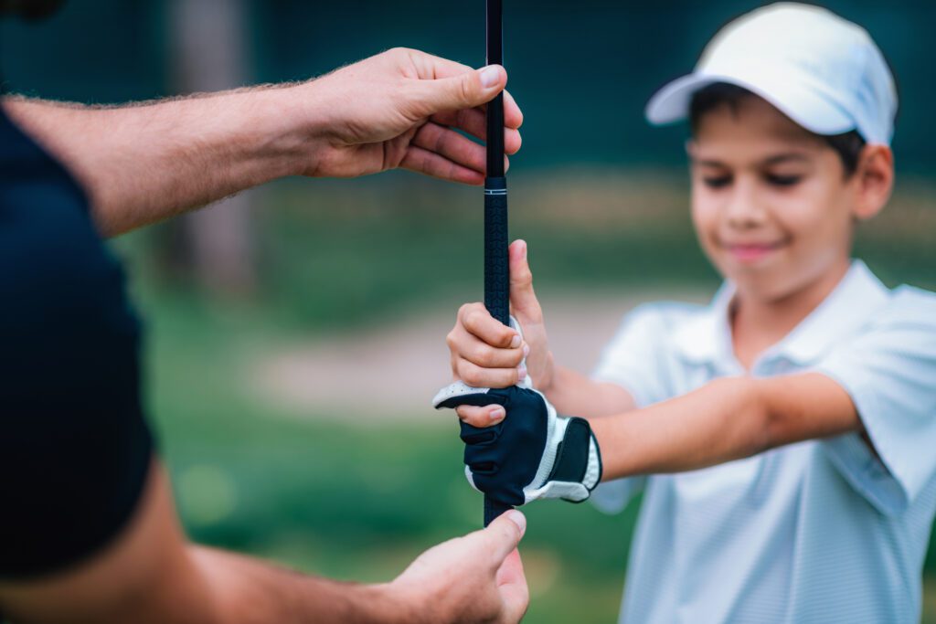 Golf Instructor adjusting young boy’s grip on golf club