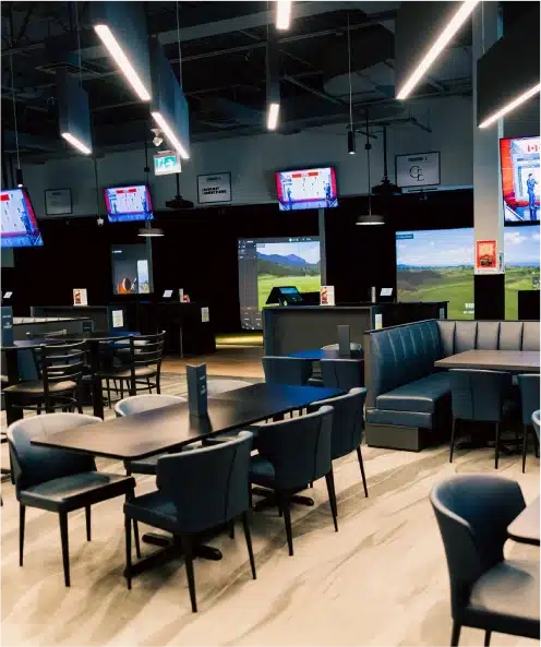 Spacious sports lounge with blue chairs, empty tables, TV screens, and TrackMan golf simulators in Kanata.