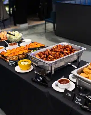 Trays of chicken wings, sliders, fried chicken, and sides set out on a black tablecloth in a golf lounge.