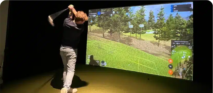 Golfer swinging a club at a large digital screen golf simulation at Silverwood’s Golf & Lounge in Kanata.