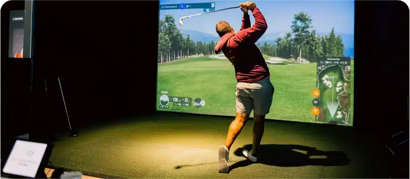 Golfer swinging a club at a large TrackMan simulator screen at Silverwoods Golf & Lounge in Kanata.